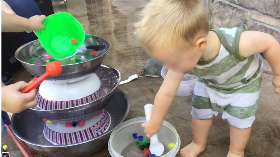 child playing with pom poms in a waterfall made of stacked bowls