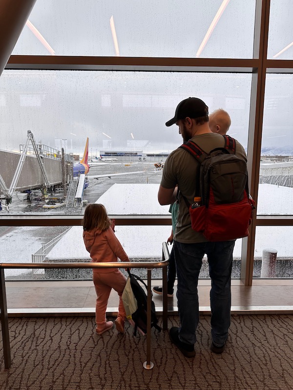 children and a father looking out a window at an airport before takeoff