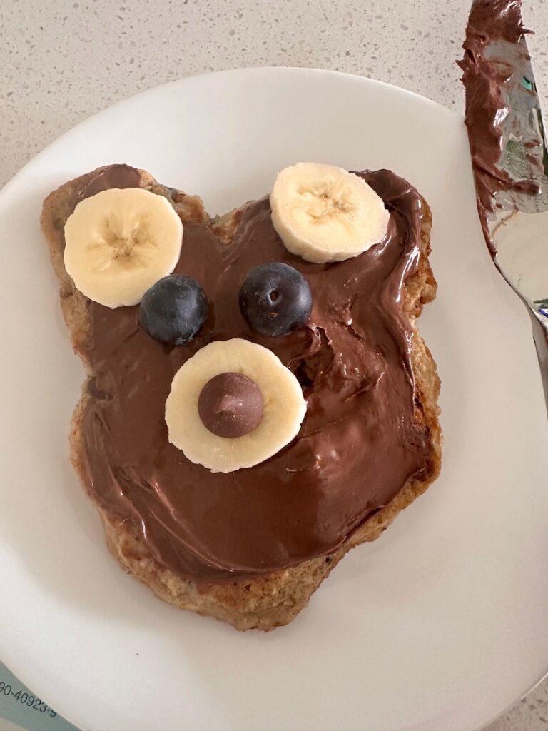 bear-shaped pancake decorated with bananas, blueberries, chocolate chips