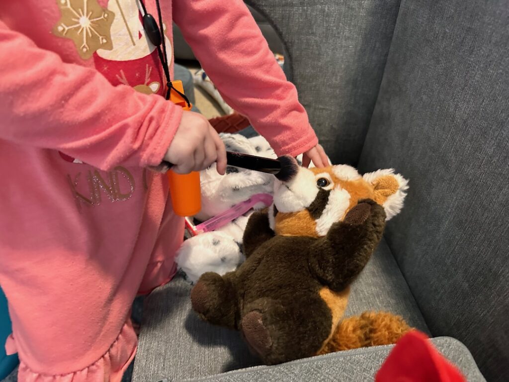 child brushing red panda stuffed animal nose with a makeup brush