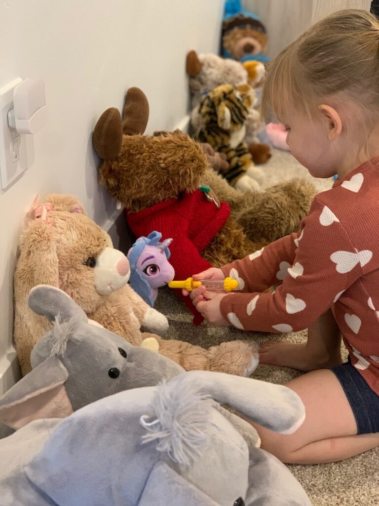 child pretending to give medicine to stuffed animals