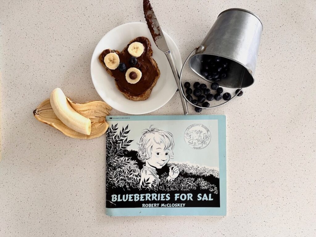 flatlay of blueberries for sal, decorated bear pancake, pail of blueberries