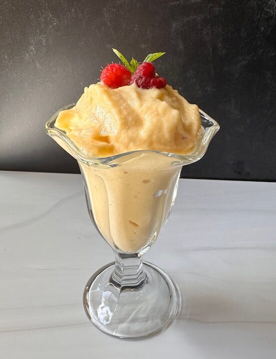 dole whip in a decorative glass garnished with raspberries and mint.