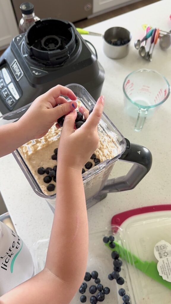 child adding blueberries to a blender