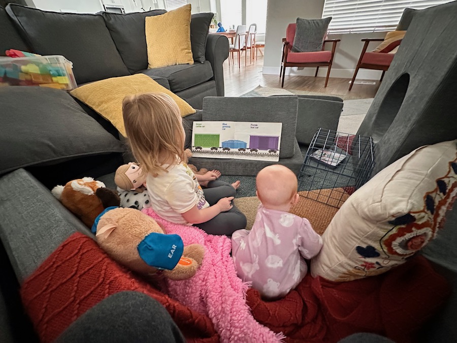 two children in a pile of couch cushions reading a book resting on a wedge pillow